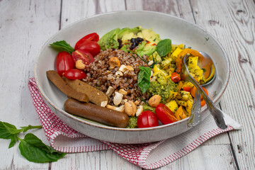 Vegan bowl consisting of pland based sausages, cooked buckwheat groats, avocado and  zucchini