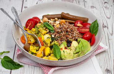 Vegan bowl consisting of plant based sausages, cooked buckwheat groats, avocado and  zucchini