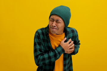 Young Asian man in a beanie hat and casual shirt is clutching his chest, displaying symptoms...