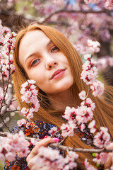 Pretty teen girl are posing in garden near blossom cherry tree with white flowers