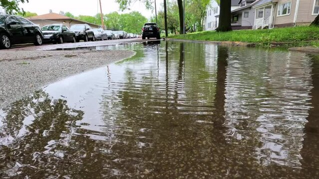 Surface level views of a flooded city street following severe weather and heavy rainfall. Cars are parked on the side of the street. City neighborhood setting. Slow motion views.