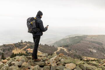 A hiker stops on a rocky hill top to get his bearings, checking GPS on phone, on a cold winter day...