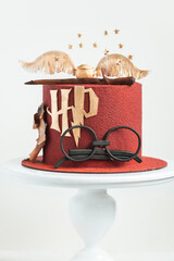 Naklejka premium KYIV, UKRAINE - March 03: Harry Potter cake on the white background. Birthday magic cake with red velvet chocolate coating decorated with mastic glasses, Elder Wand and Golden Snitch
