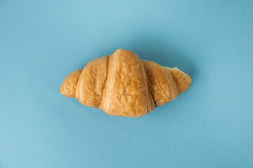 Flat lay of single freshly baked croissant on the blue pastel background. Traditional French pastry with a copy space for a free text