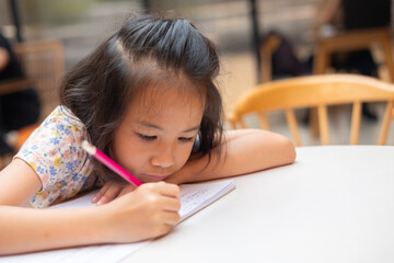 Face and eyes close up of adorable Asian kid girl who is writing with determination and...