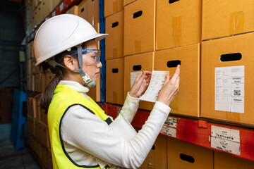 Beautiful Asian woman puts a barcode sticker on a cardboard box in a warehouse.