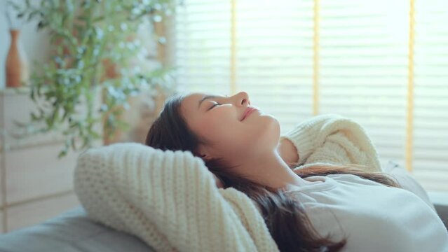 Relaxed young asian woman on comfortable sofa at home, female enjoying carefree peaceful weekend relaxation time alone in living room.