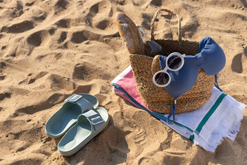 Jute bag with swim wear, sunglasses, beach towel and flip flops on the sand. Summer vacation lifestyle concept	
