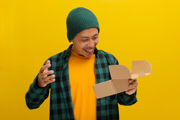 An excited Asian man, dressed in a beanie hat and casual shirt, eagerly unpacks the cardboard...