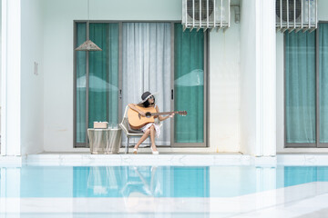 the swimming pool of a luxury hotel, an Asian woman tourist happily strums her guitar and sings,...