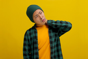 Unhealthy Asian man, dressed in a beanie hat and casual outfit, massages his neck, expressing pain...