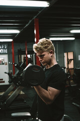 Vertical shot of a handsome muscular male athlete exercising with weights, doing biceps curls