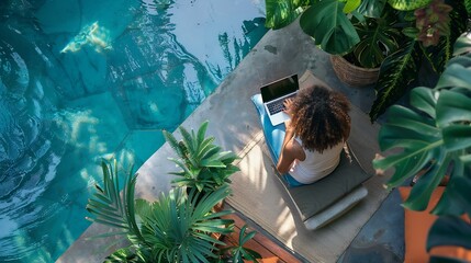 bird view of a remote online working digital nomad women with curly hair and laptop sitting at a sunny turquoise water pool surrounded by cushions and plants in the foreground : Generative AI