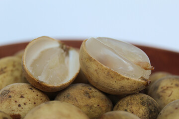 Fruit of Lansium domesticum var duku, known as duku, or langsat, or lanzones, on wooden plate, isolated on white background