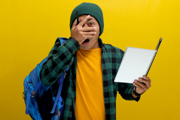 Funny Asian student, wearing a beanie hat and casual clothes, carrying a backpack, appears shocked...