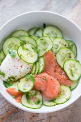 Cucumber salad with smoked salmon and poached egg served in a white bowl, vertical shot, middle close-up, selective focus