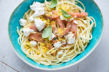 Lemony spaghetti with smoked salmon, feta cheese and basil in a turquoise bowl, horizontal shot,...