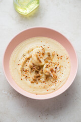 Roseate bowl with cream-soup made of roasted cauliflower, vertical shot on a light-beige stone background