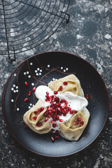 Manty or steamed asian dumplings with yogurt and pomegranate seeds on a black plate, vertical shot on a dark-brown granite background, high angle view
