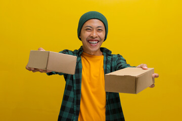 A smiling Asian man, dressed in a beanie hat and casual shirt, holds a stack of package parcel...