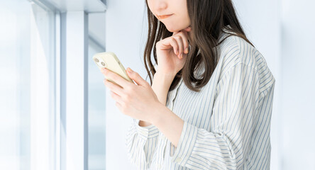 スマートフォンを見ながら考える若い女性