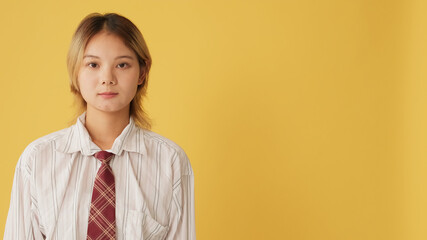 Close-up, young woman dressed in shirt stands and looks at the camera camera isolated on yellow...