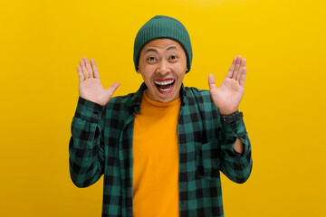 Excited young Asian man, dressed in a beanie hat and casual shirt, is expressing joy and...