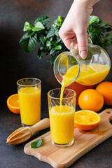Orange juice is poured into a glass. Orange juice in a glass on a dark background