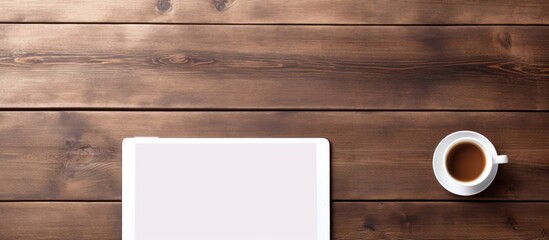 Top view of a vintage style wooden table adorned with a white tablet computer displaying a blank screen Accompanied by a cup of black coffee notepads pencils and a calculator the image offers ample c