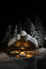 The frame of a house under construction in a Siberian forest illuminated by a lamp in the night with a huge mass of snow lying on the roof