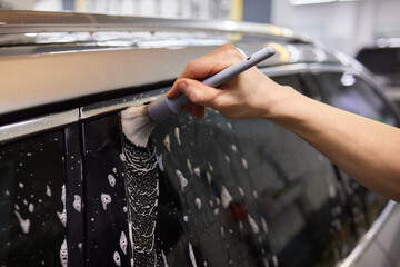 A person is cleaning a car windshield with a brush and water