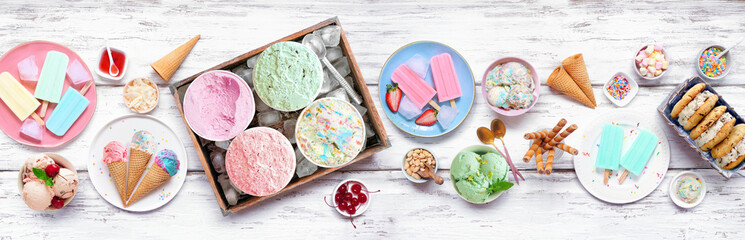Cool summer food table scene. Assortment of ice cream, popsicles and frozen treats. Pastel colors. Above view on a white wood banner background.