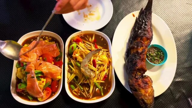 Top View Thai Food on the Table: Isaan Food (Somtam - Papaya Salad, Grilled Catfish, Salmon Salad) Local and Traditional Ways Background Thai Food Enjoy eating ideas with amazing flavors. - video