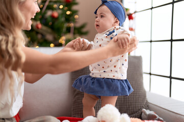 Woman and toddler standing on sofa by christmas tree at home