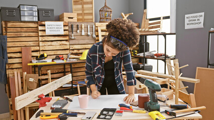 Hispanic woman with curly hair working attentively in a carpentry studio room.