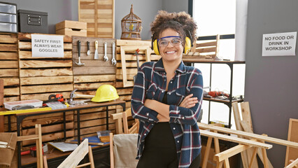 Smiling young hispanic woman with curly hair wearing safety goggles stands arms crossed in a...