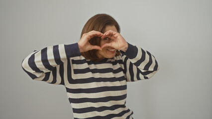 A middle-aged woman forms heart shape with hands, smiling, isolated on white background.