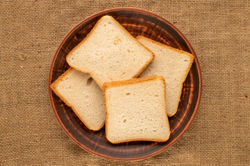Several pieces of white toaster bread on a clay plate on a jute cloth, macro, top view.