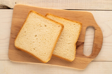 Two pieces of white bread for toaster with wooden kitchen board on wooden table, macro, top view.