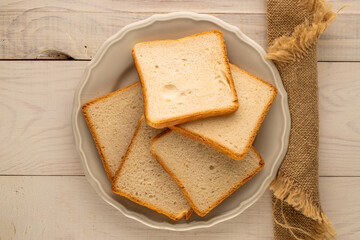 Several pieces of white bread for toaster with ceramic plate on wooden table, macro, top view.