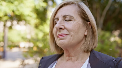 Mature caucasian woman with closed eyes enjoying peace in a lush green park setting.