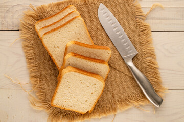 Several pieces of white bread for toaster with jute napkin and knife on wooden table, macro, top...