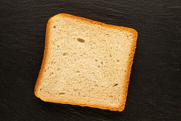 One slice of white toaster bread on a slate stone, macro, top view.