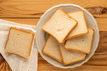 Several pieces of white bread for toaster with ceramic plate on wooden table, macro, top view.
