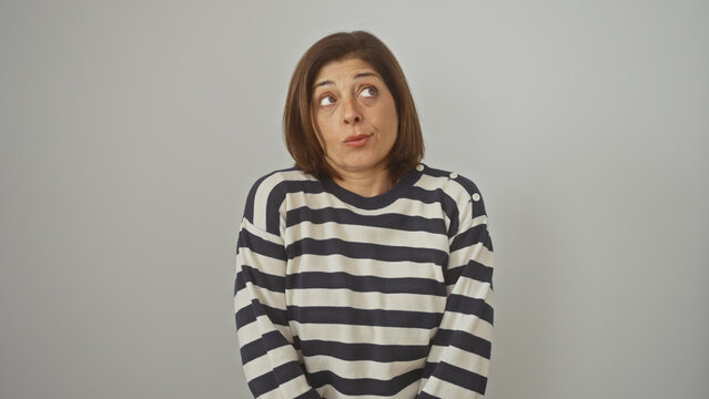 A middle-aged hispanic woman in a striped sweater poses with a quizzical expression against an isolated white wall.