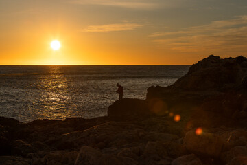 hombre pescando en playa de rocas al amanecer