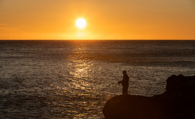 hombre pescando en playa de rocas al amanecer