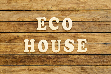 The inscription Eco house made of wooden letters on a wooden background, top view.