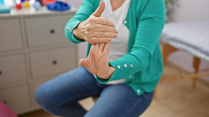 A mature blonde woman stretching her fingers indoors at a rehab clinic, symbolizing hand therapy...