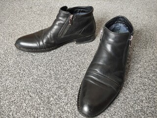 Worn black men's leather low shoes on a background of gray carpet